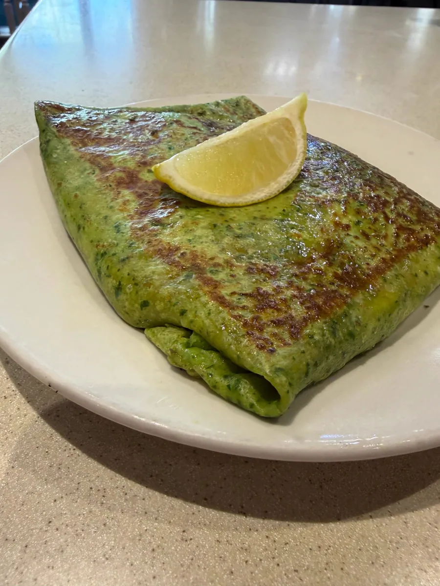 Folded green spinach crêpe with a lemon wedge